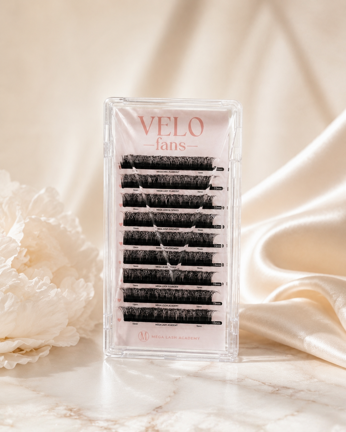 VELO false eyelash fans in a clear rectangular plastic case, displayed on a marble surface with soft cream fabric and a white flower in the background.