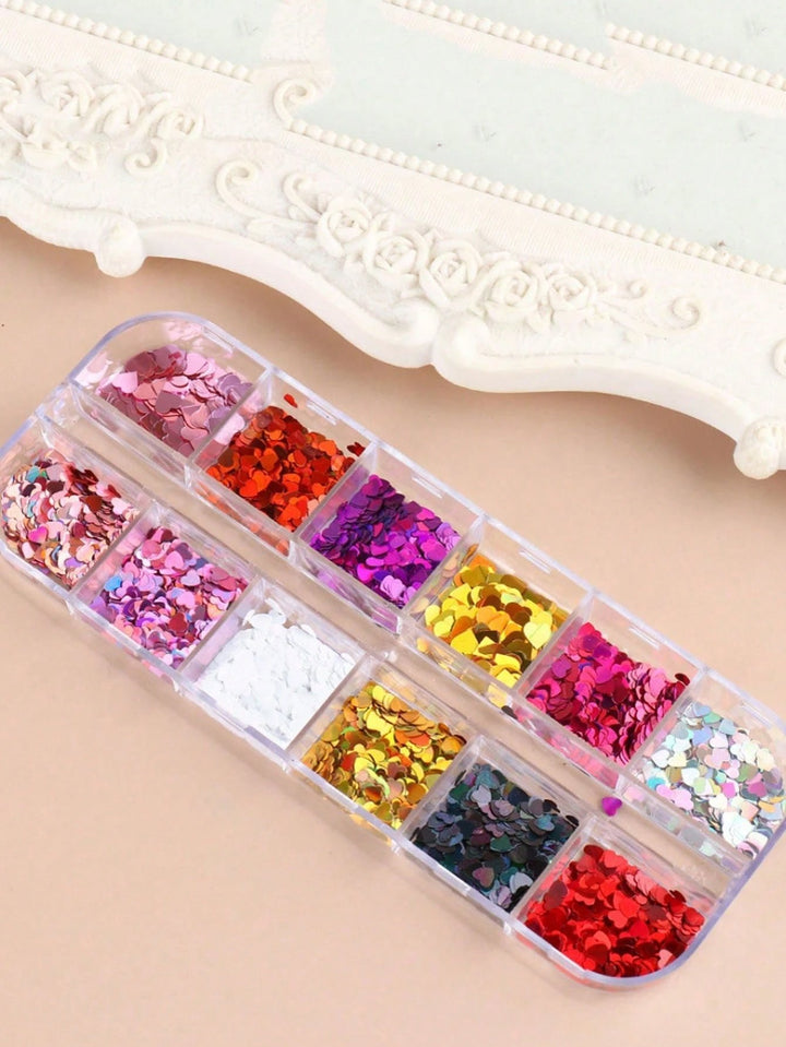 A clear plastic organizer tray filled with assorted decorative glitter flakes in multiple colors, including pink, red, purple, gold, silver, and dark blue, arranged on a light beige surface with a white ornate frame in the background.